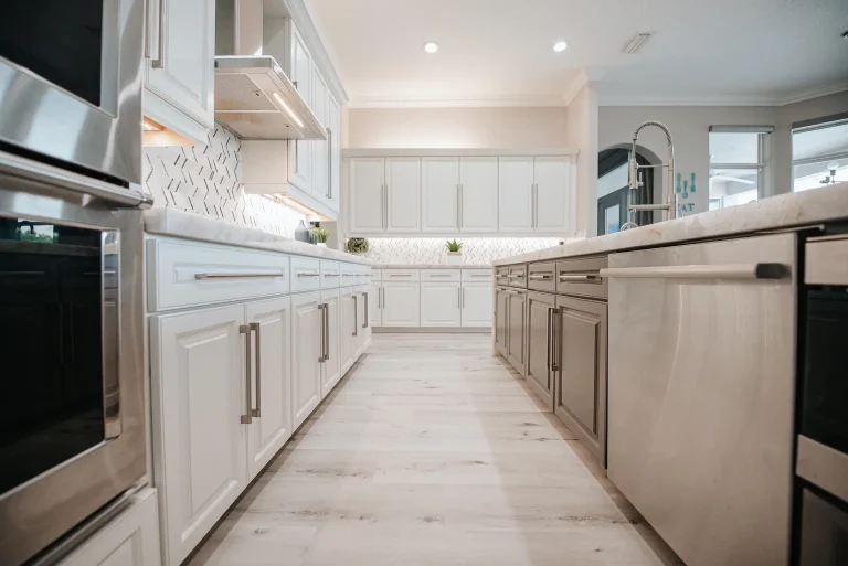 Modern white kitchen with quartz countertops, herringbone backsplash, stainless steel appliances and light wood floors