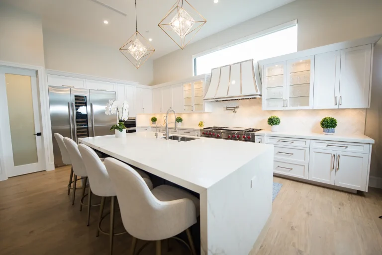 Modern white kitchen design with quartz waterfall island, white bar stools, geometric pendant lights, and light wood floors