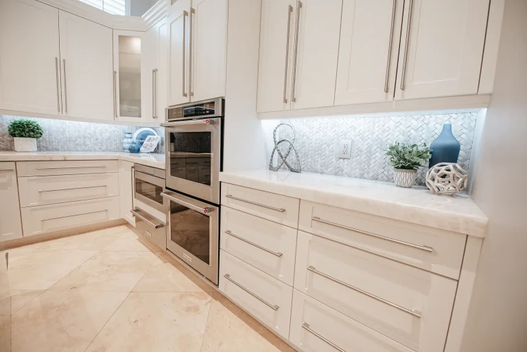 Modern white kitchen with quartz countertops, herringbone backsplash, stainless steel appliances and open shelving by YOLO Interiors Fort Lauderdale