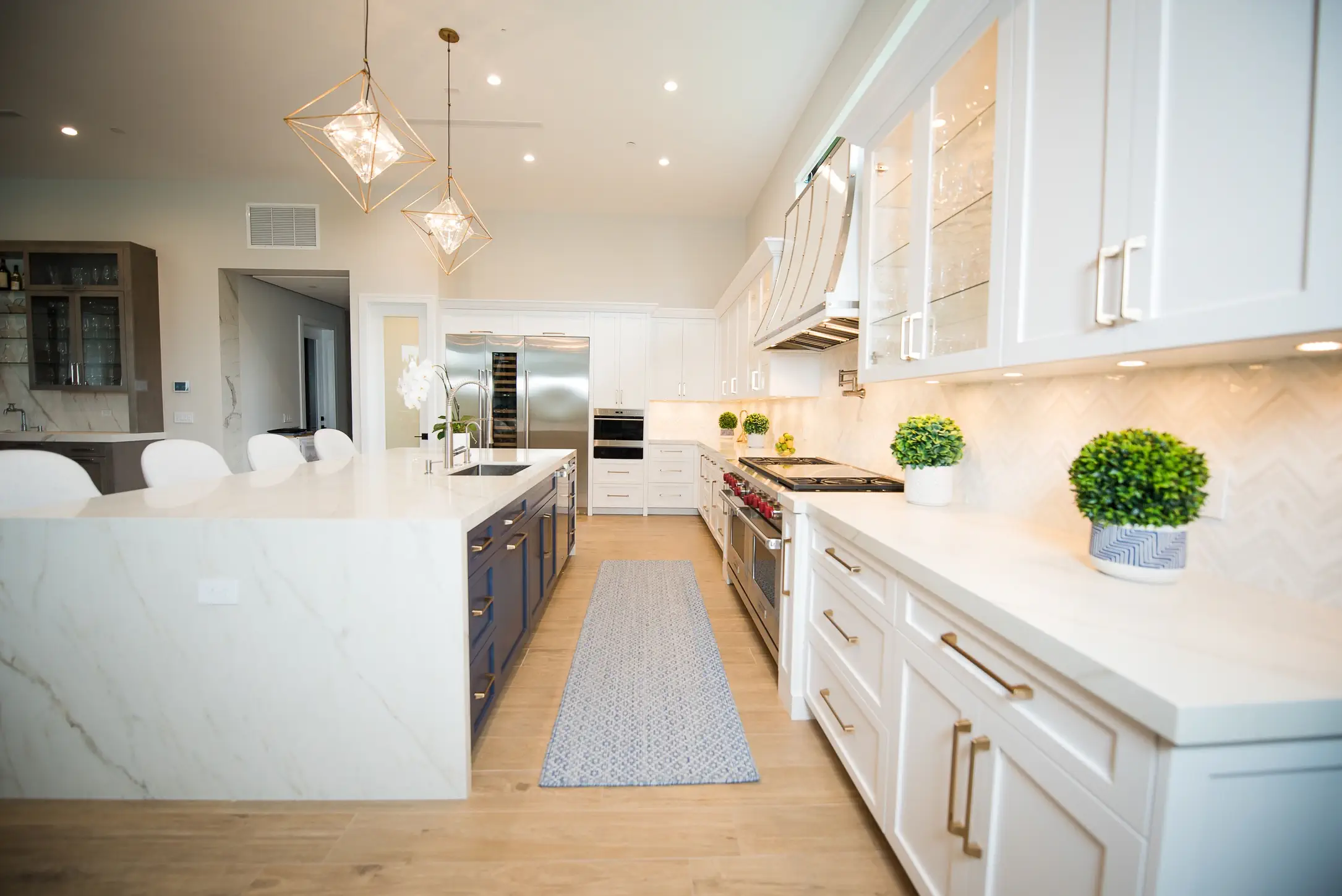 Modern white kitchen with quartz countertops, gold hardware, geometric pendant lights, and light wood floors in Fort Lauderdale home