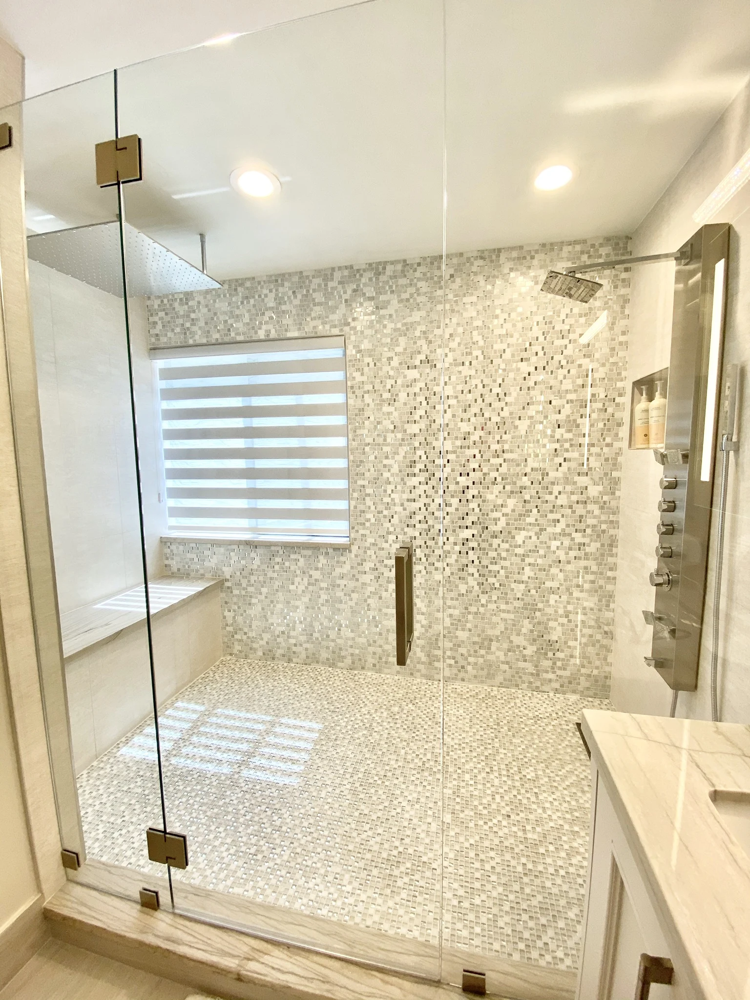 Luxury walk-in shower with white mosaic tile walls, glass doors, rainfall showerhead, and built-in bench seat