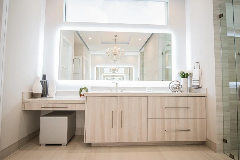 Modern bathroom vanity with light wood cabinets, white marble countertop, LED mirror, and crystal chandelier in luxury Fort Lauderdale home