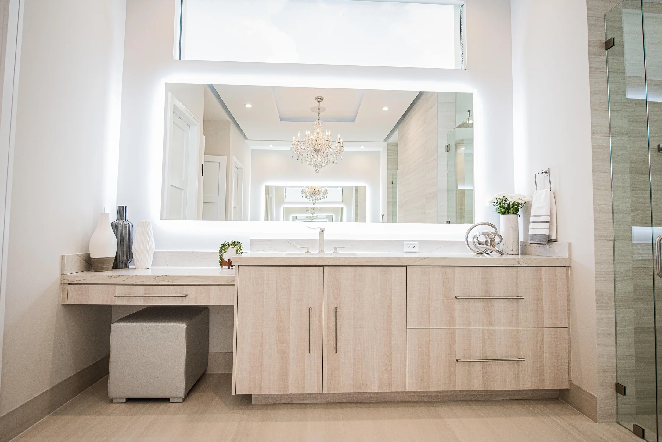 Modern bathroom vanity with light wood cabinets, white marble countertop, LED mirror, and crystal chandelier in luxury Fort Lauderdale home