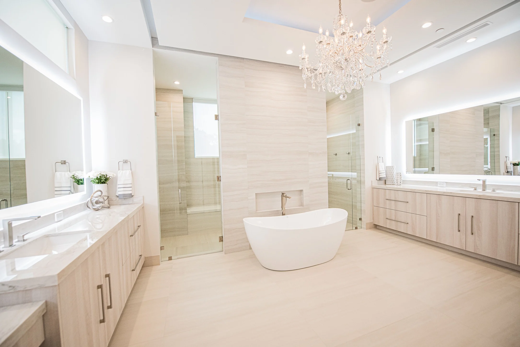 Luxury master bathroom with white freestanding tub, crystal chandelier, marble countertops, light wood vanities Fort Lauderdale interior design